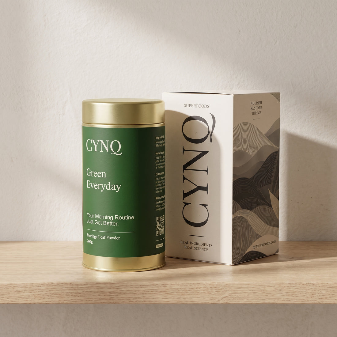 Green Everyday moringa powder tin beside the CYNQ outer box on an oak shelf