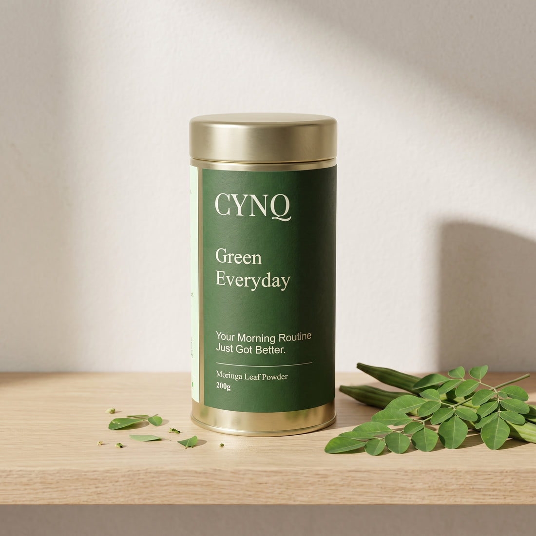 Green Everyday tin on an oak shelf with fresh moringa leaves