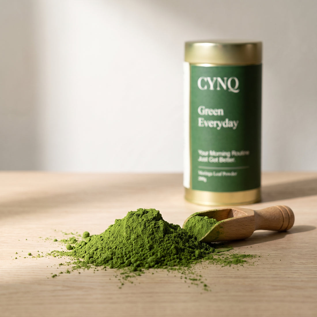 Bright green moringa leaf powder heaped beside a wooden scoop, with a blurred Green Everyday tin behind
