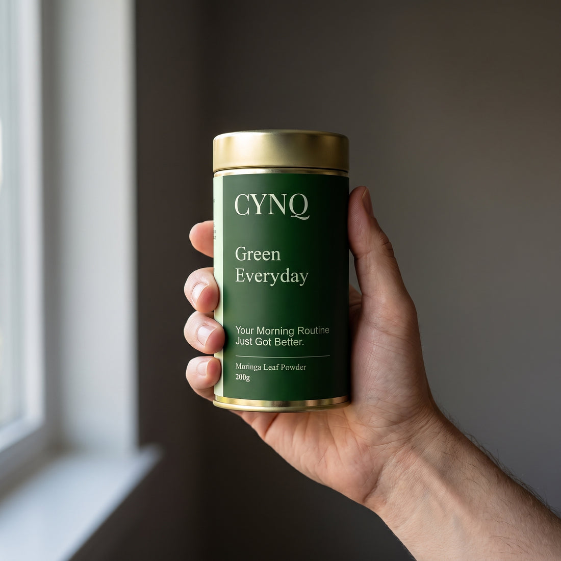 Hand holding a Green Everyday moringa powder tin with the label facing the camera