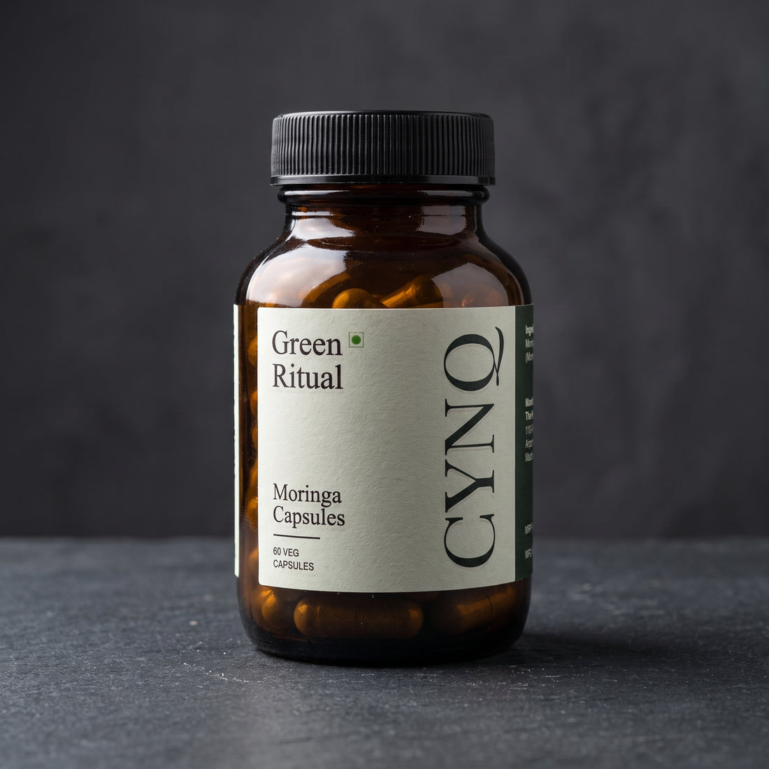 Green Ritual moringa extract capsules in an amber glass bottle with a cream CYNQ label, on a dark slate surface