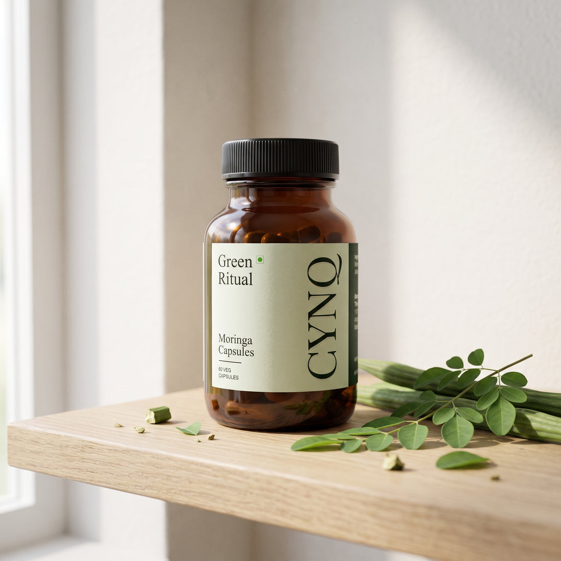 Green Ritual capsule bottle on an oak shelf with fresh moringa leaves and pods
