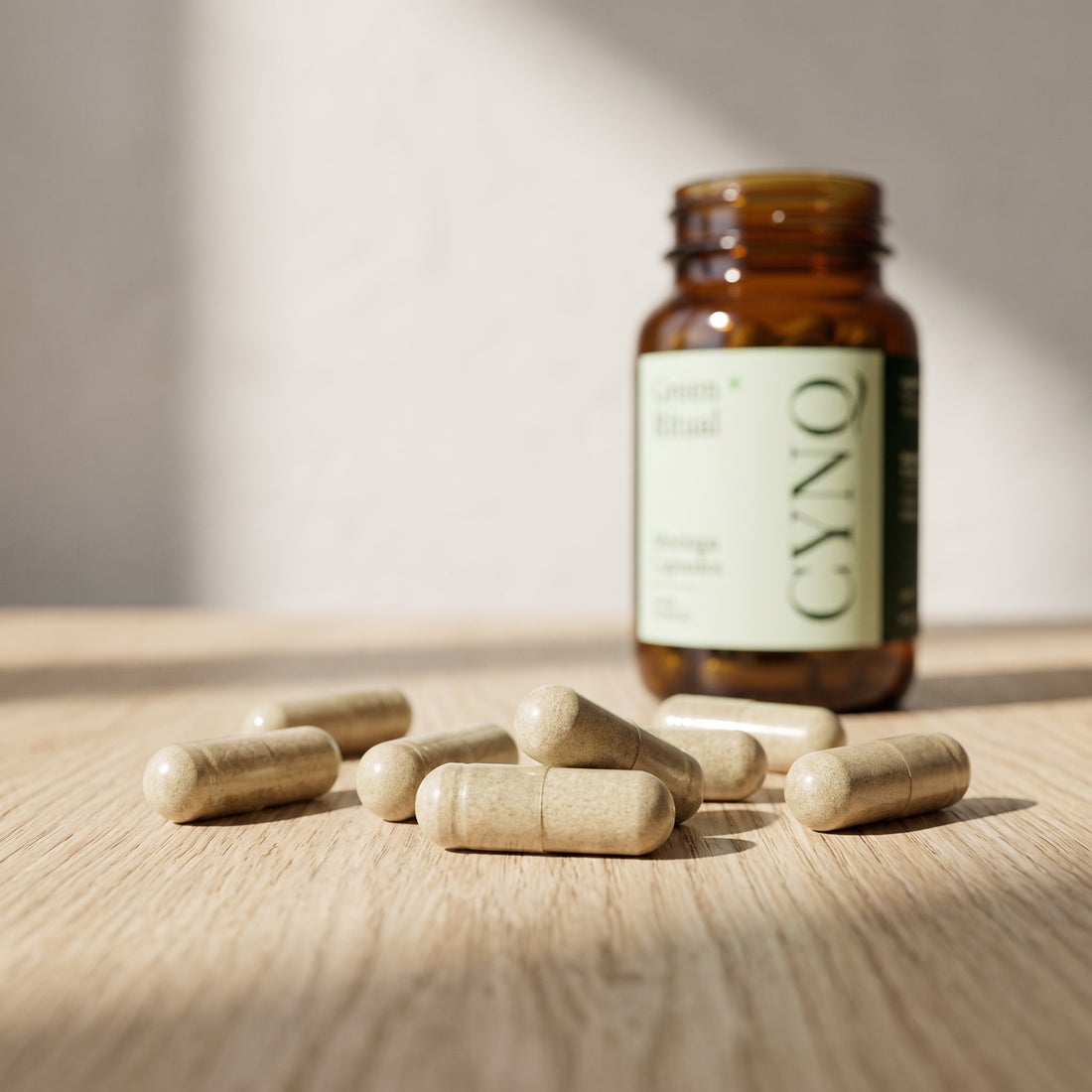Moringa capsules scattered on an oak surface with a blurred Green Ritual bottle behind