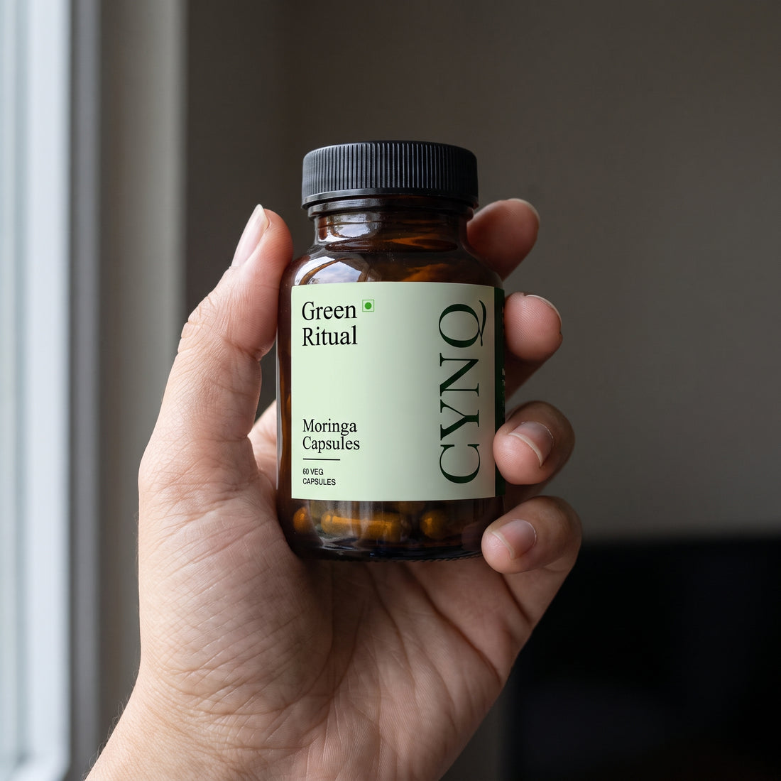 Hand holding a Green Ritual moringa capsule bottle with the label facing the camera