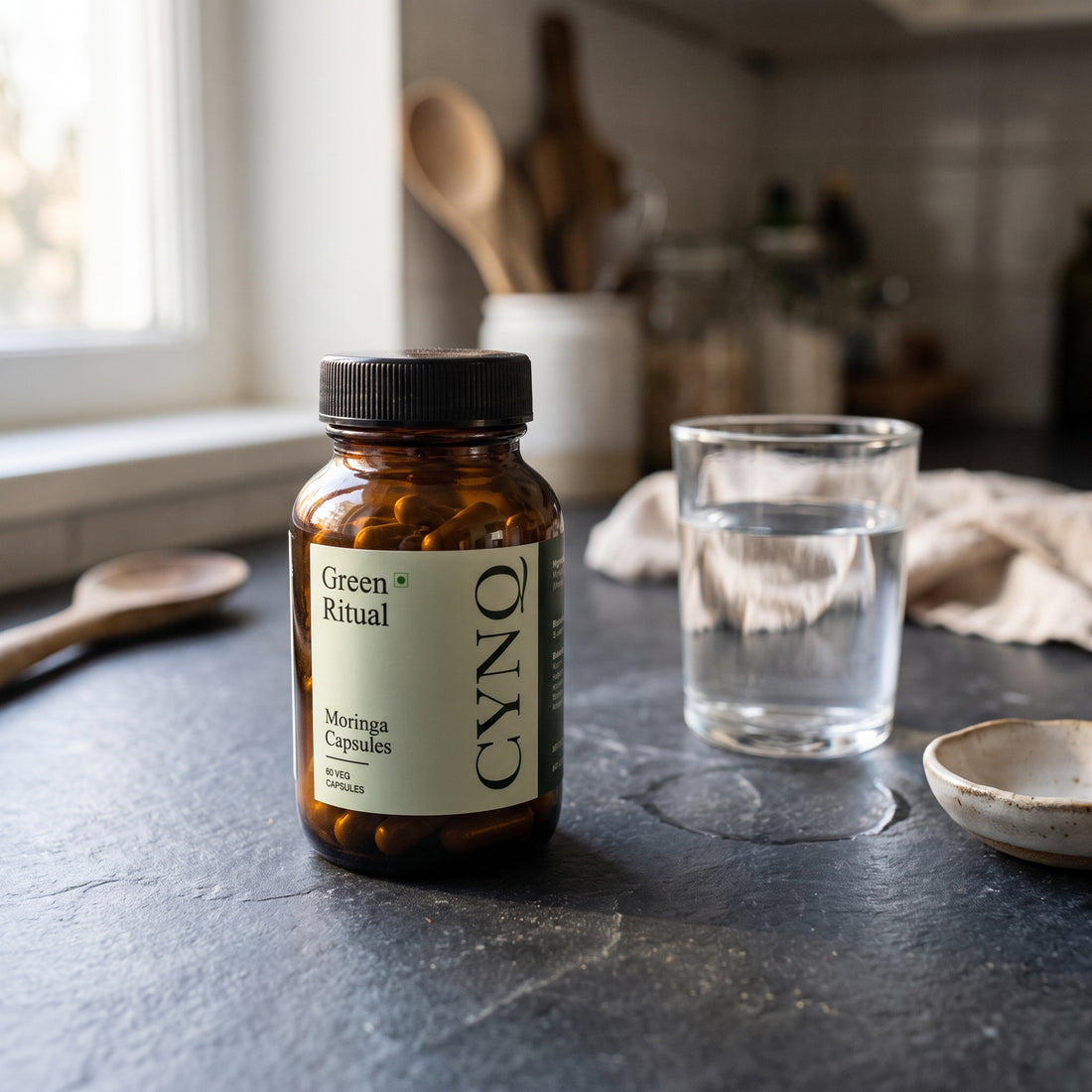 Green Ritual capsule bottle on a dark stone counter next to a glass of water and a ceramic dish