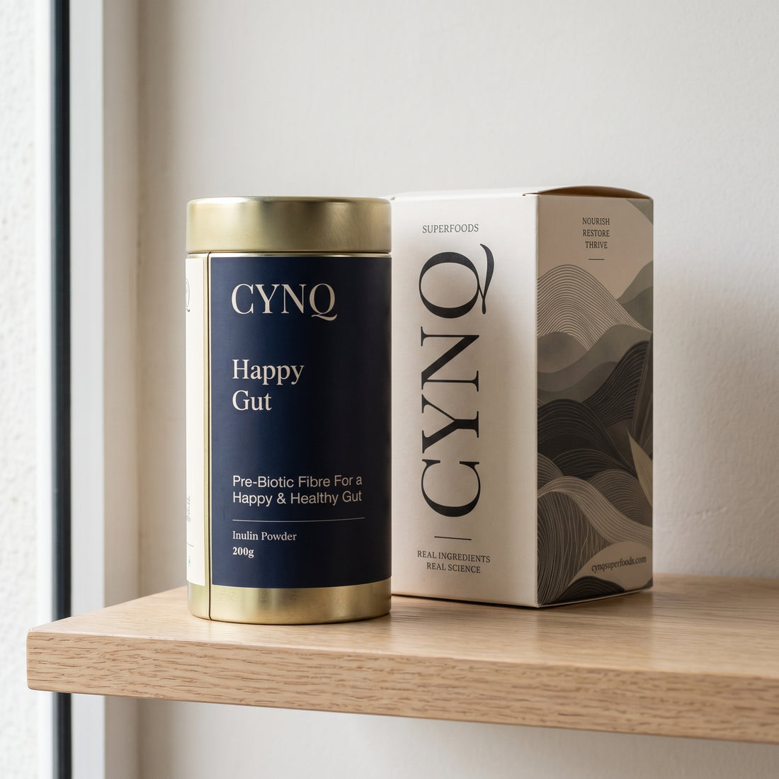 Happy Gut inulin tin beside the CYNQ outer box on an oak shelf by a window