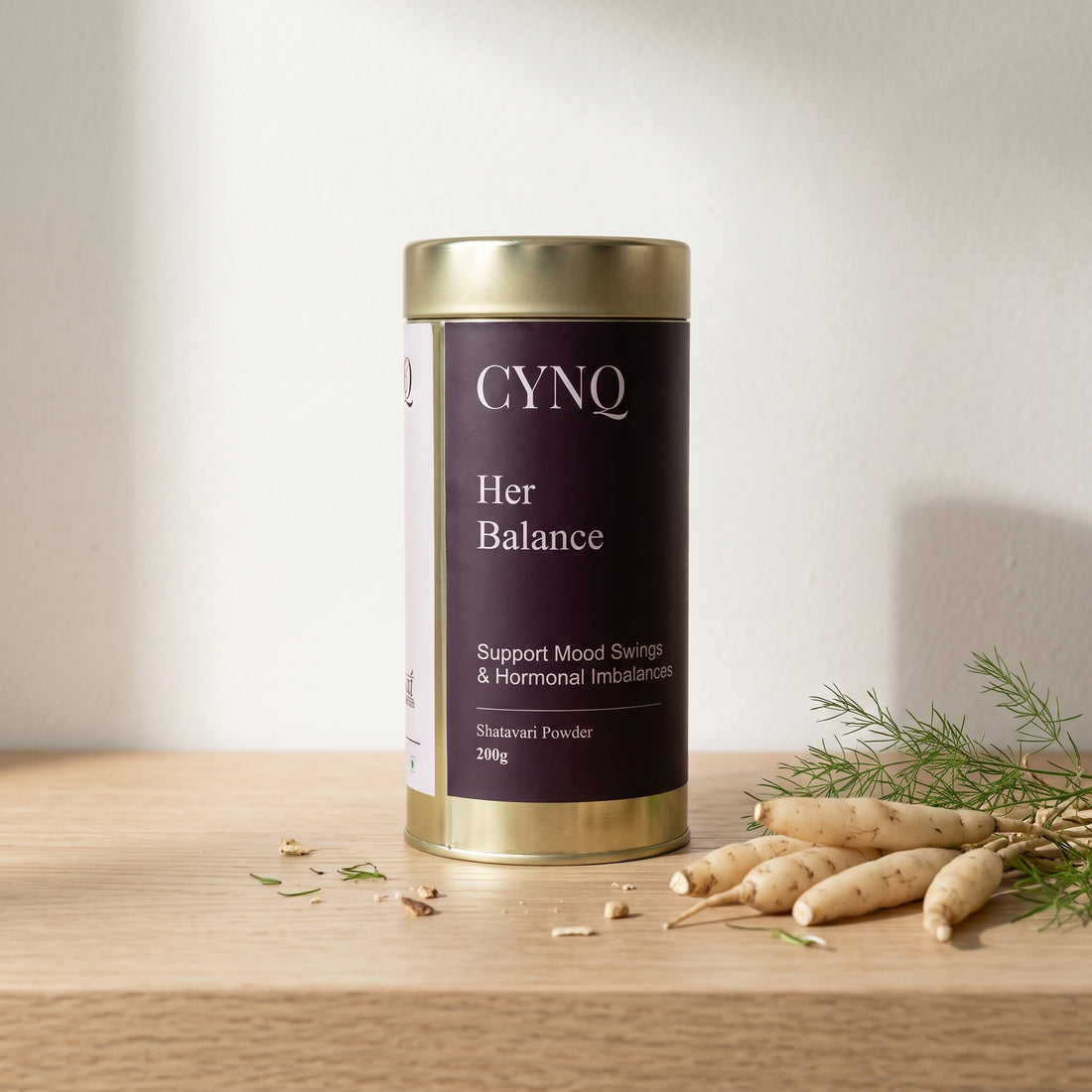 Her Balance tin on an oak shelf with fresh shatavari roots and a green sprig
