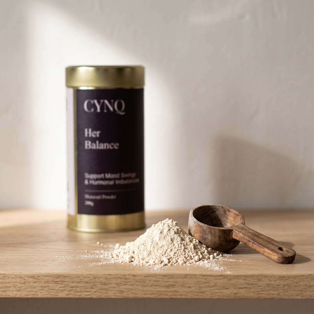 Pale shatavari root powder with a wooden spoon and a blurred Her Balance tin behind
