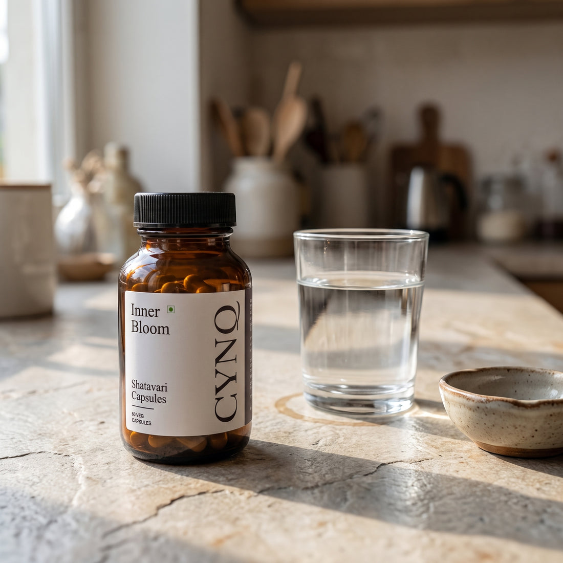 Inner Bloom capsule bottle on a sunlit stone counter with a glass of water and a small ceramic bowl