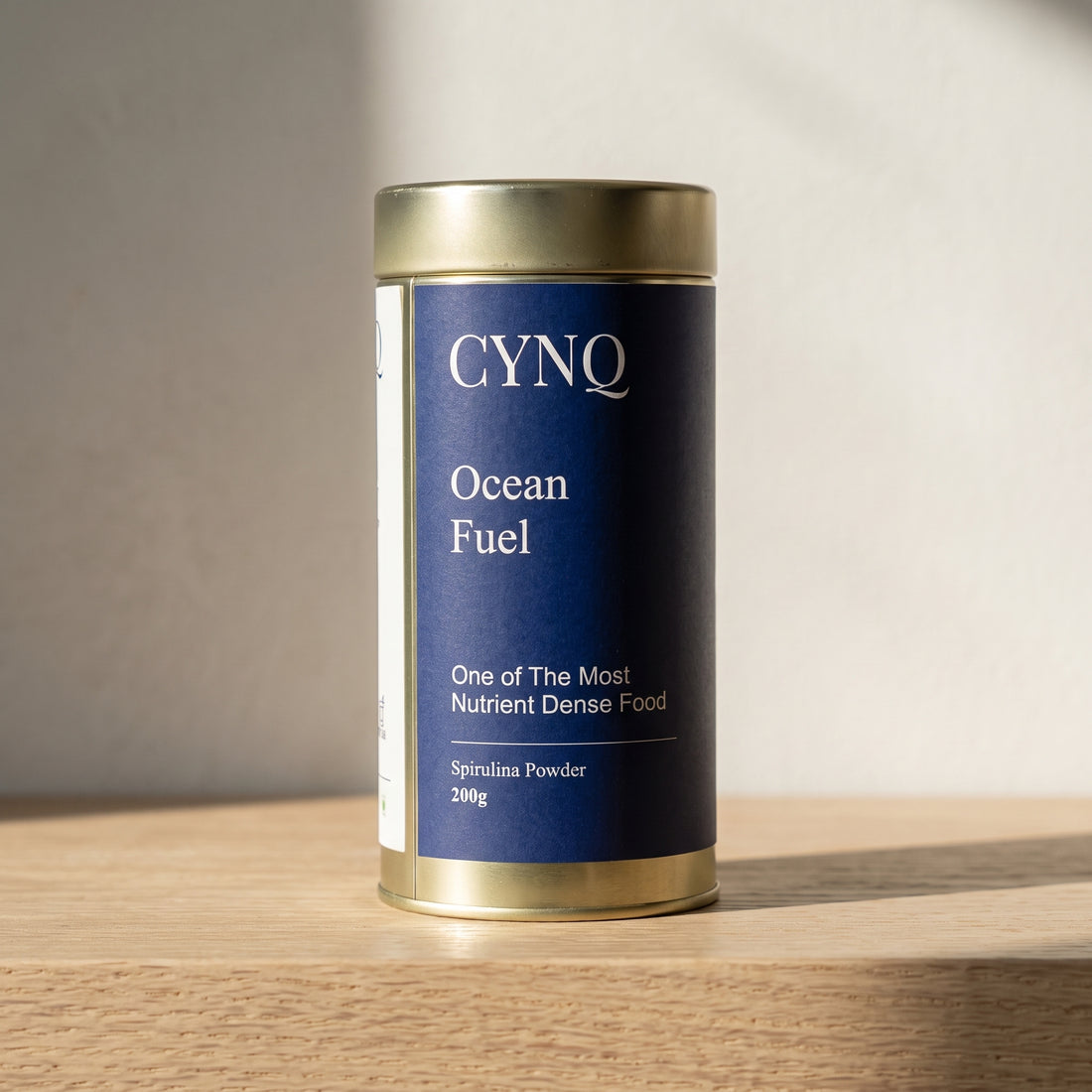 Ocean Fuel spirulina powder tin, front view, on an oak shelf in soft light