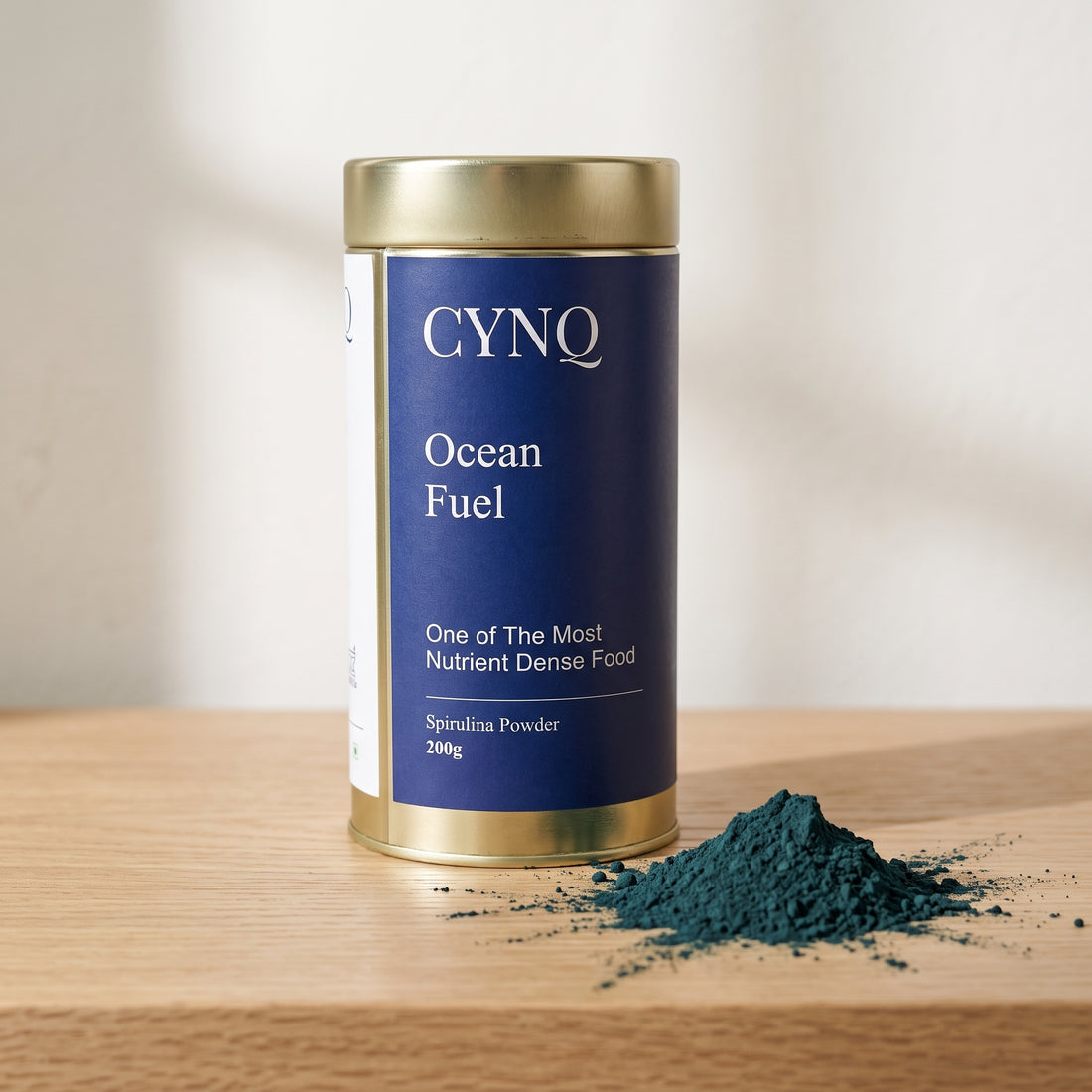 Ocean Fuel tin on an oak shelf with a small pile of dark green spirulina powder