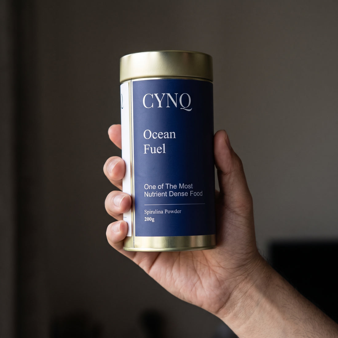 Hand holding an Ocean Fuel spirulina powder tin with the label facing the camera