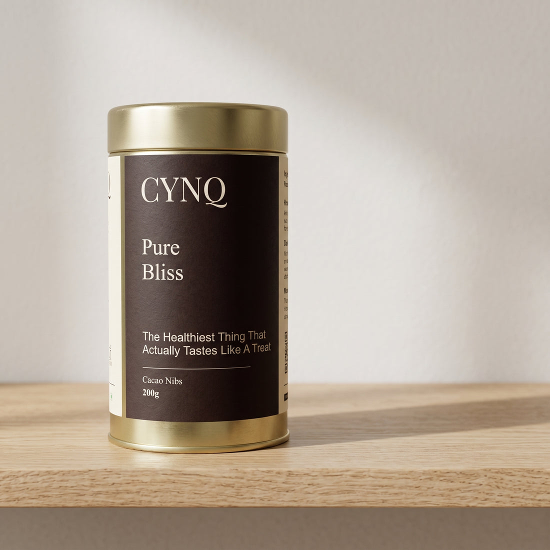 Pure Bliss cacao nibs in a gold tin with a dark brown CYNQ label, on an oak shelf