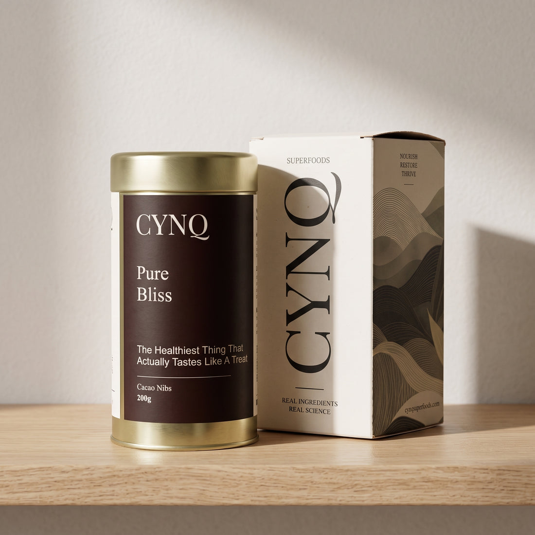 Pure Bliss cacao nibs tin beside the CYNQ outer box on an oak shelf