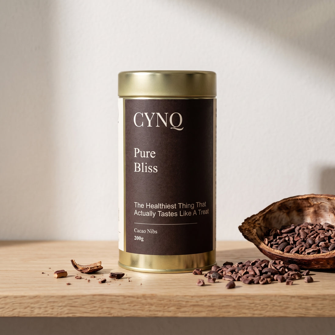 Pure Bliss tin on an oak shelf with a cacao pod husk and scattered cacao nibs