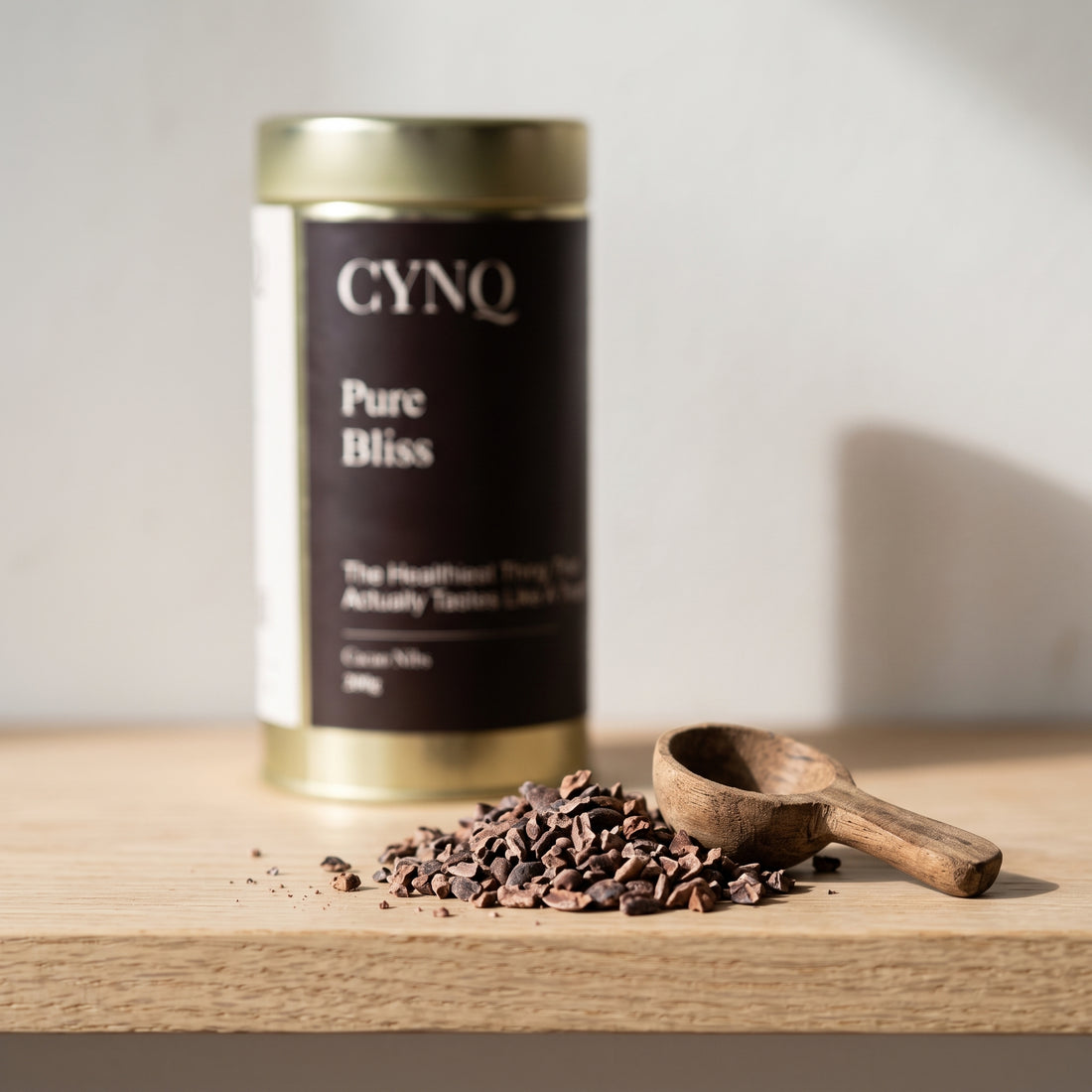 Cacao nibs with a wooden scoop and a blurred Pure Bliss tin behind