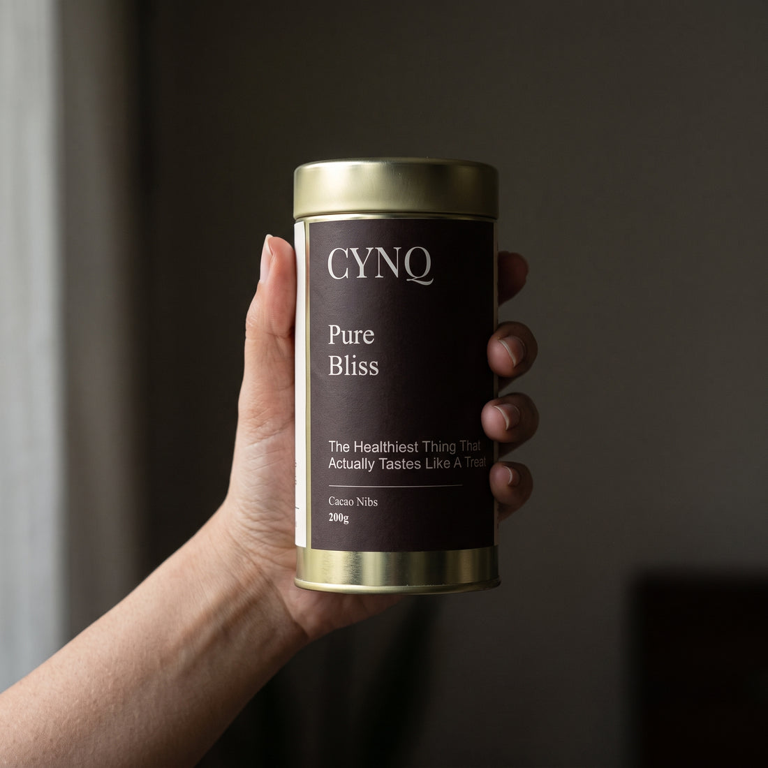 Hand holding a Pure Bliss cacao nibs tin with the label facing the camera