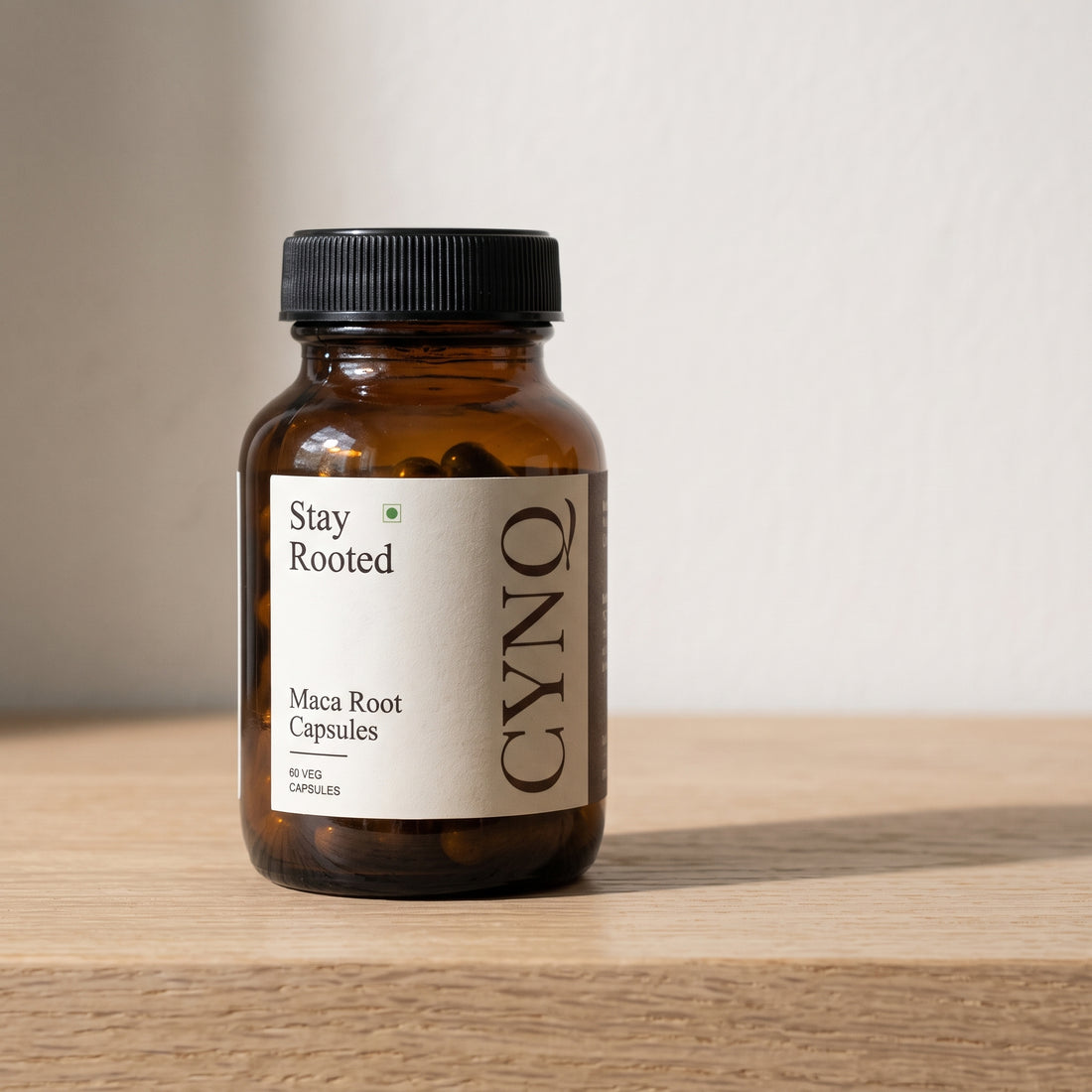 Stay Rooted maca root capsules in an amber glass bottle with a cream CYNQ label, on an oak shelf