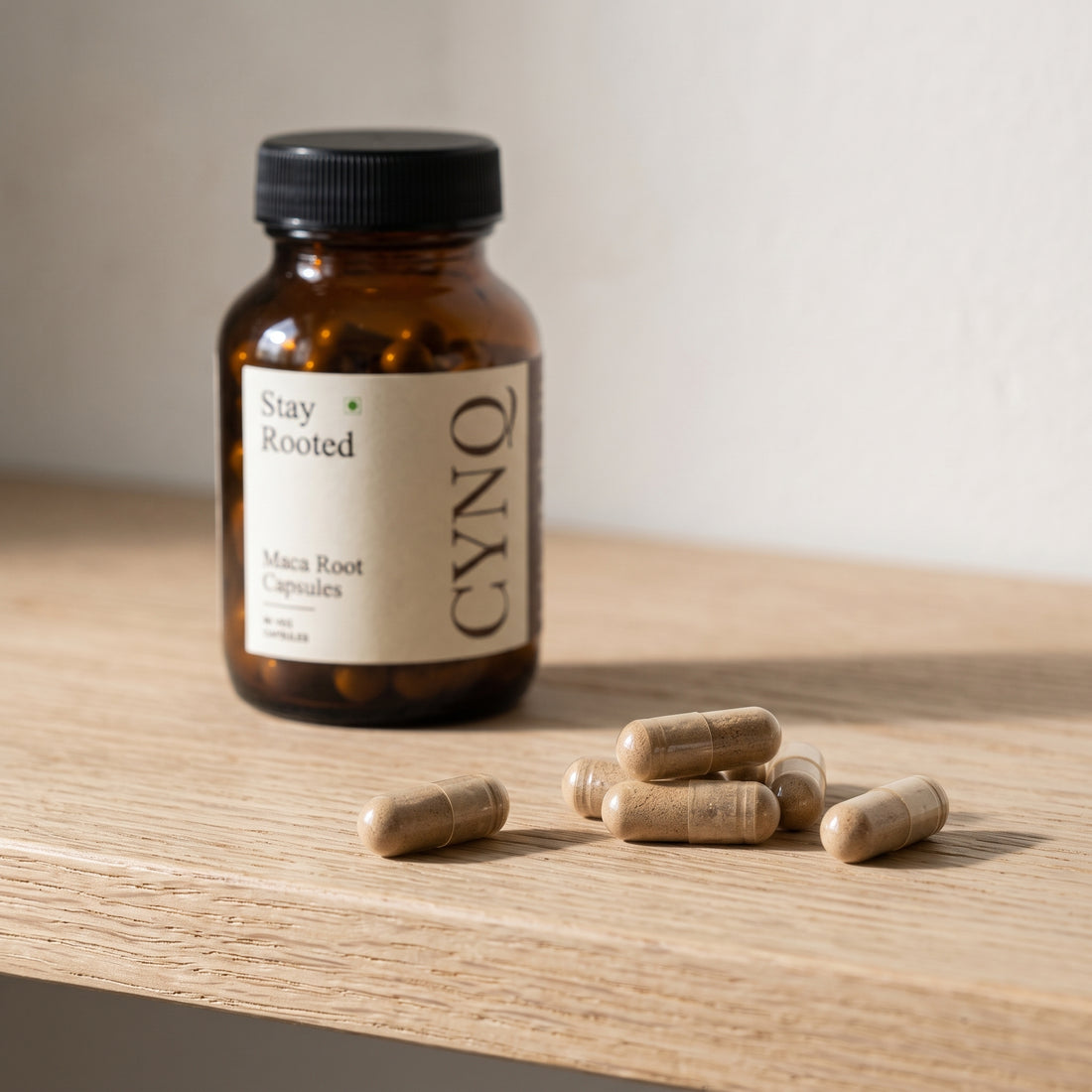 Maca capsules on an oak shelf with a blurred Stay Rooted bottle behind