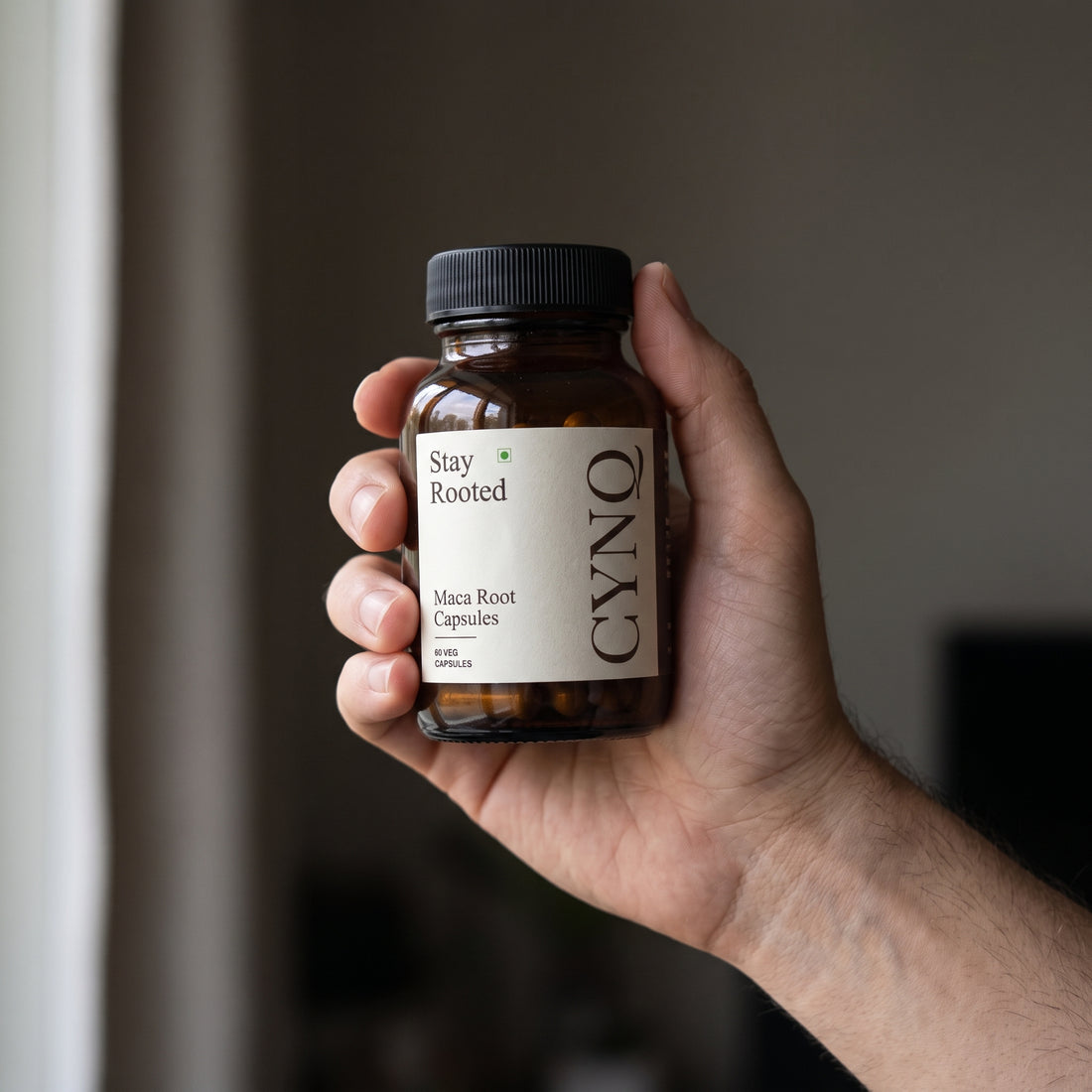 Hand holding a Stay Rooted maca capsule bottle with the label facing the camera