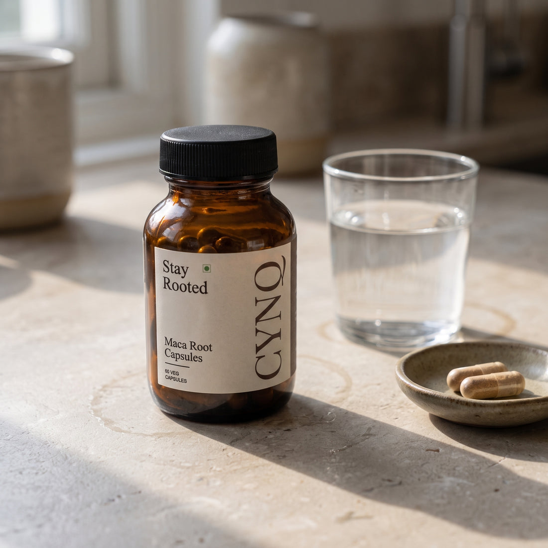 Stay Rooted capsule bottle on a stone counter with a glass of water and a dish of capsules